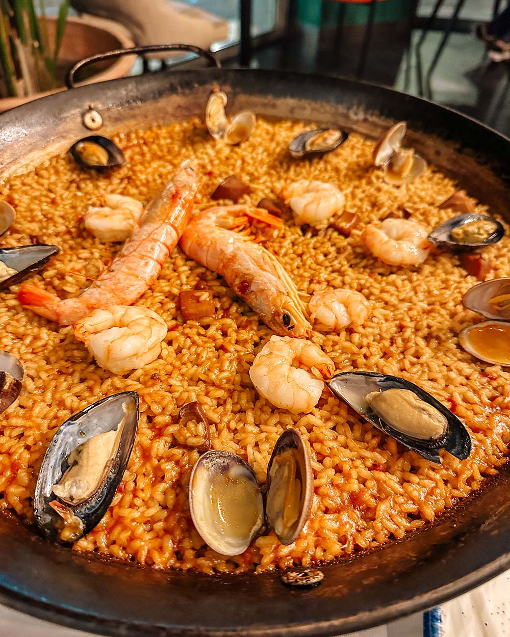 Seafood paella in a large cast-iron pan with shrimp and mussels on top.