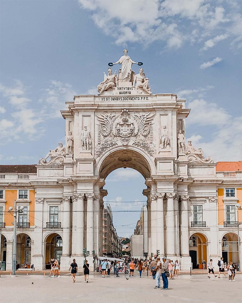Tall Rua Augusta Arch with surrounding yellow buildings, crowd and square.
