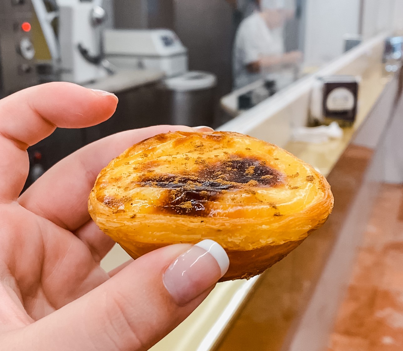 Patel de nata, creamy custard tart at Mantegeira. Workers behind prep more pastries.
