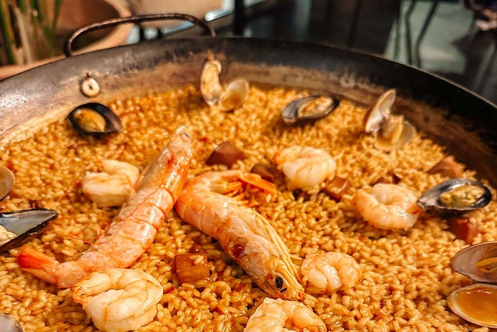 Seafood paella in a large cast-iron pan with shrimp and mussels on top.