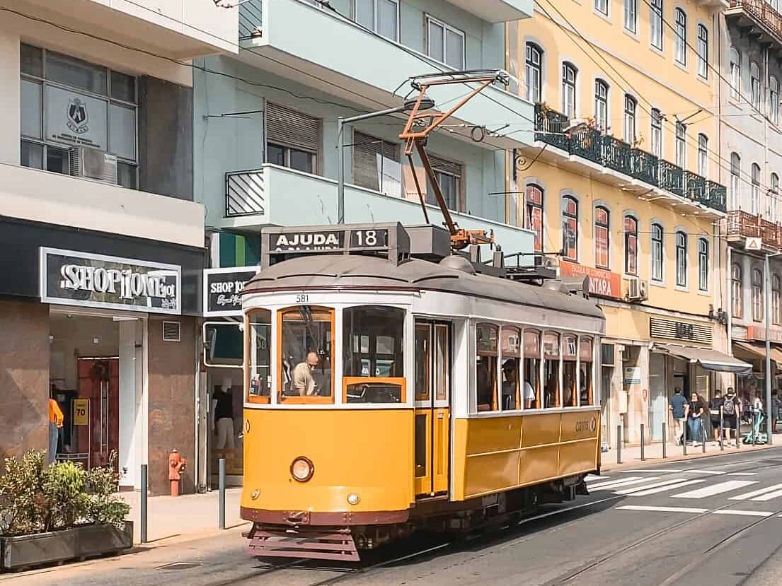 Lisbon's historic yellow tram passing through a neighborhood with pastel buildings.