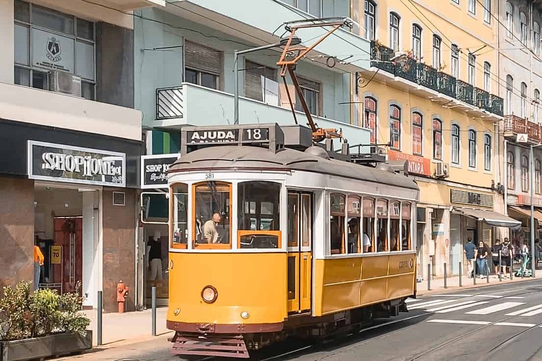Yellow tram passes through street in front of blue building.